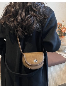 Close-up of a vintage brown suede saddle bag worn on shoulder with silver metal buckle