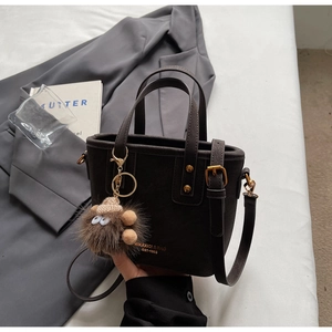 Detail of dark brown leather tote bag with plush monster charm and adjustable strap
