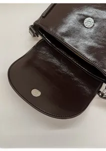 Close-up of secure magnetic clasp on vintage dark brown leather crossbody saddle bag