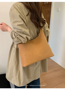 Close-up of a large minimalist khaki matte tote bag worn by a model in a warm room