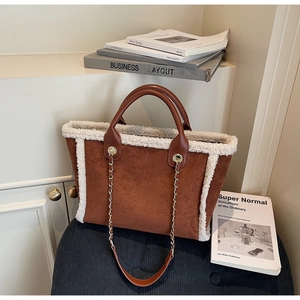 Close-up of brown suede tote bag featuring white faux shearling trim and metal chain strap