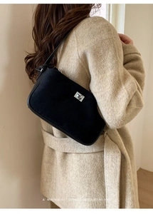 Detailed view of a black suede underarm bag with silver metal swivel lock on a wool coat