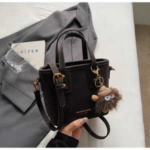 Close-up of coffee brown tote bag with fuzzy monster charm and metallic hardware