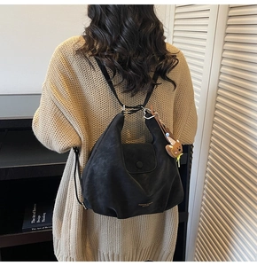 Détail du sac à bandoulière en cuir noir avec bouton pression et breloque ours mignon