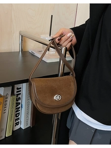 Close-up of brown suede saddle bag with silver twist lock held by model in retro setting