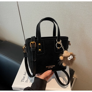 Detail of black matte leather tote with golden branding and cute plush monster charm