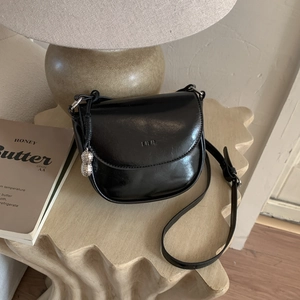 Detail of a black glossy saddle bag with LILIL logo and silver fruit charm on a stylish table
