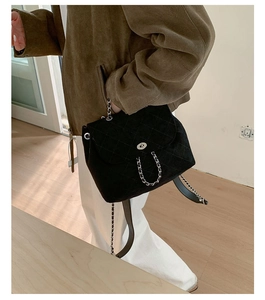 Detail of a black quilted backpack featuring a silver twist lock and chain strap