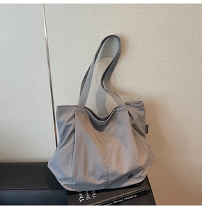 Detail of grey pleated tote bag featuring side brand label and wide woven shoulder strap