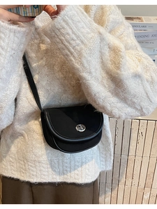 Close-up of black saddle crossbody bag featuring a round silver metal twist lock buckle