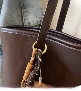 Detail einer dunkelbraunen Ledertasche mit goldenen Ringen und gewebtem Ornament