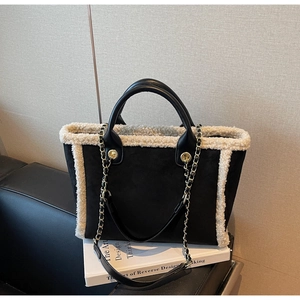 Close-up of black suede tote bag with cream faux shearling trim and gold chain strap detail