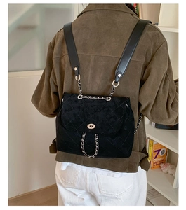 Detail of black quilted velvet backpack with metal chain straps and turn-lock closure
