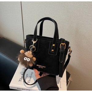 Close-up of black matte tote bag with golden hardware and a brown fuzzy monster charm