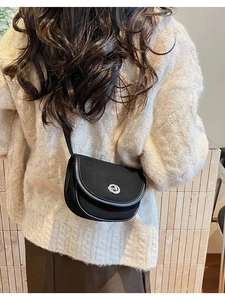 Detail of a black matte saddle bag featuring a silver floral metal clasp on a beige sweater