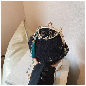 Detail of vintage floral embroidery and green tassel on a black shell-shaped handbag