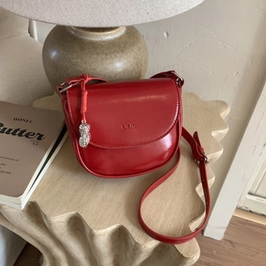 Detail of red glossy leather saddle bag featuring a unique silver peanut pendant
