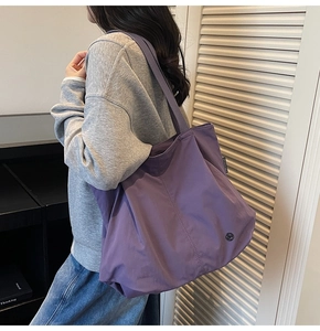 Large purple tote bag shoulder strap and brand label detail in casual urban setting