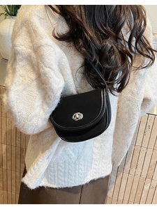 Detail view of a black saddle crossbody bag with silver twist lock on a white sweater