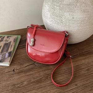 Detail of red glossy leather saddle bag with silver peanut charm on wooden desk