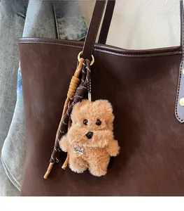 Detail eines braunen Plüschhund-Anhängers mit Perlenkette an einer Ledertasche