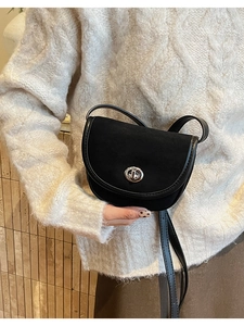 Detail of black matte saddle bag with silver turn-lock clasp on white knit sweater