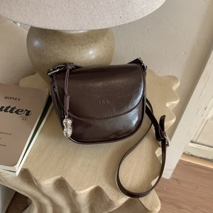Detailed view of dark brown faux leather saddle bag with silver peanut charm and logo embossing