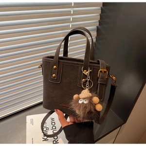 Detail of dark brown bucket bag with gold hardware and cute plush monster charm