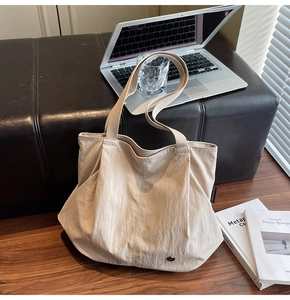 Detail view of beige nylon tote bag with wide strap and side brand label on wood floor