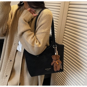 Gros plan d'un grand sac cabas noir mat avec surpiqûres blanches et pendentif ours en peluche