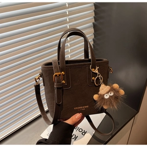 Close-up of matte dark brown bucket bag with gold lettering and a plush monster charm