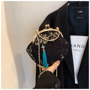 Detail of black vintage embroidery shell bag with golden floral patterns and green tassel