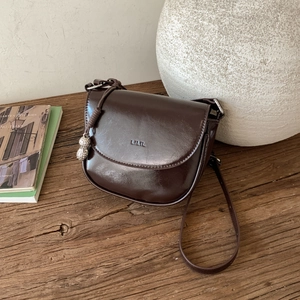 Deep brown saddle bag with metal peanut charm and LILIL logo on premium glossy leather