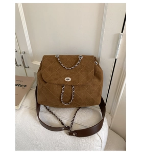 Detail of dark coffee quilted suede crossbody bag with silver twist lock on tweed sofa