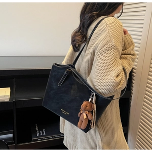 Gros plan du sac cabas noir texturé avec logo doré et petit pendentif ours doux