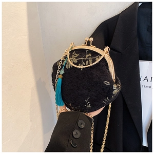 Detail of black embroidered shell bag with gold leaf patterns and a turquoise tassel