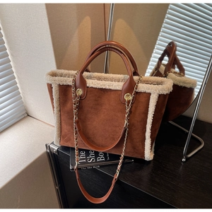 Detail of brown suede tote bag with white faux shearling trim and golden chain strap