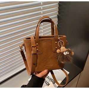 Detailed view of brown matte leather tote bag with monster charm and metal rivets