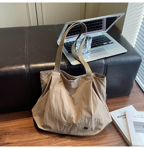 Detail of khaki tote bag with textured fabric, brown shoulder strap and minimalist side tag