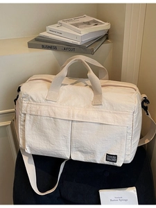 Large cream travel duffel bag with front pockets and adjustable strap on a sofa