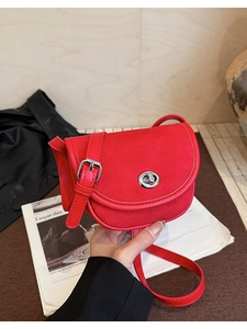 Detail of red saddle bag featuring suede paneling and a rotating metal lock closure