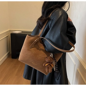 Détail du sac fourre-tout en daim marron avec breloque ours et texte vintage