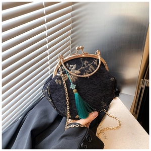 Detailed view of black shell bag with gold embroidery, metal clasp, and green tassel