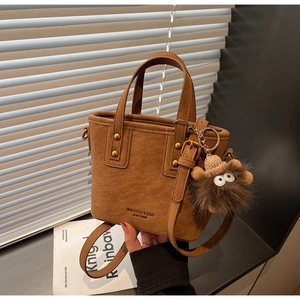 Close-up of caramel brown tote bag with litchi texture, logo detail and plush pendant