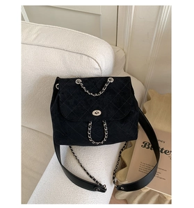 Close-up of black quilted velvet bucket bag with silver chain on a beige sofa