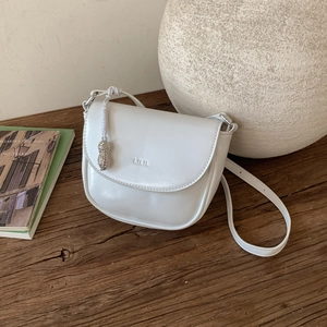 Detail of white leather saddle bag with LILIL logo and unique metal peanut pendant