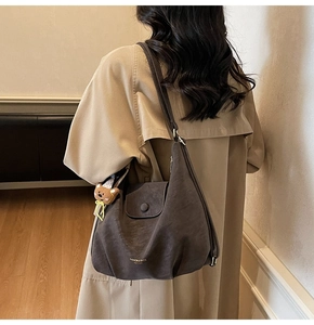 Détail d'un grand sac à bandoulière en cuir mat gris foncé avec un porte-clé ours mignon