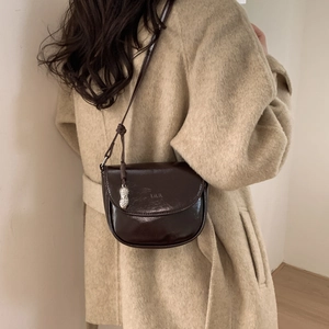 Detail of dark brown glossy saddle bag with unique silver peanut shaped metal pendant