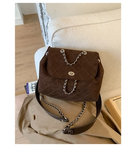 Detailed view of brown quilted suede backpack with silver twist lock and chain on a sofa