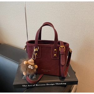 Close-up of wine red leather bucket bag with gold logo and plush monster charm decoration